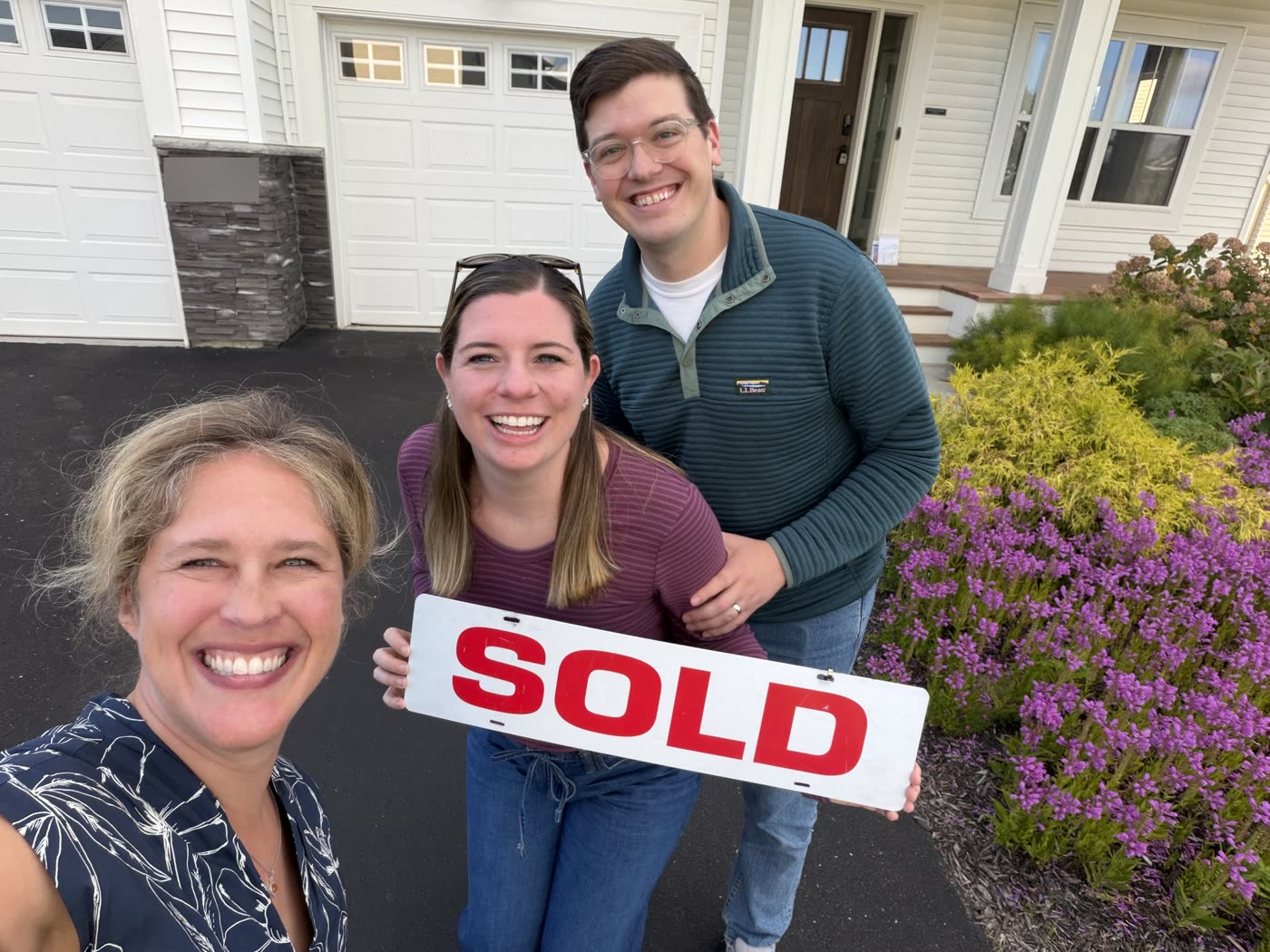 Andrea Scanlon taking a selfie with two smiling clients holding a SOLD sign outside their new home