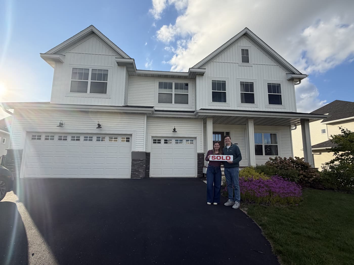 Two clients holding a SOLD sign in the driveway of their new two-story home