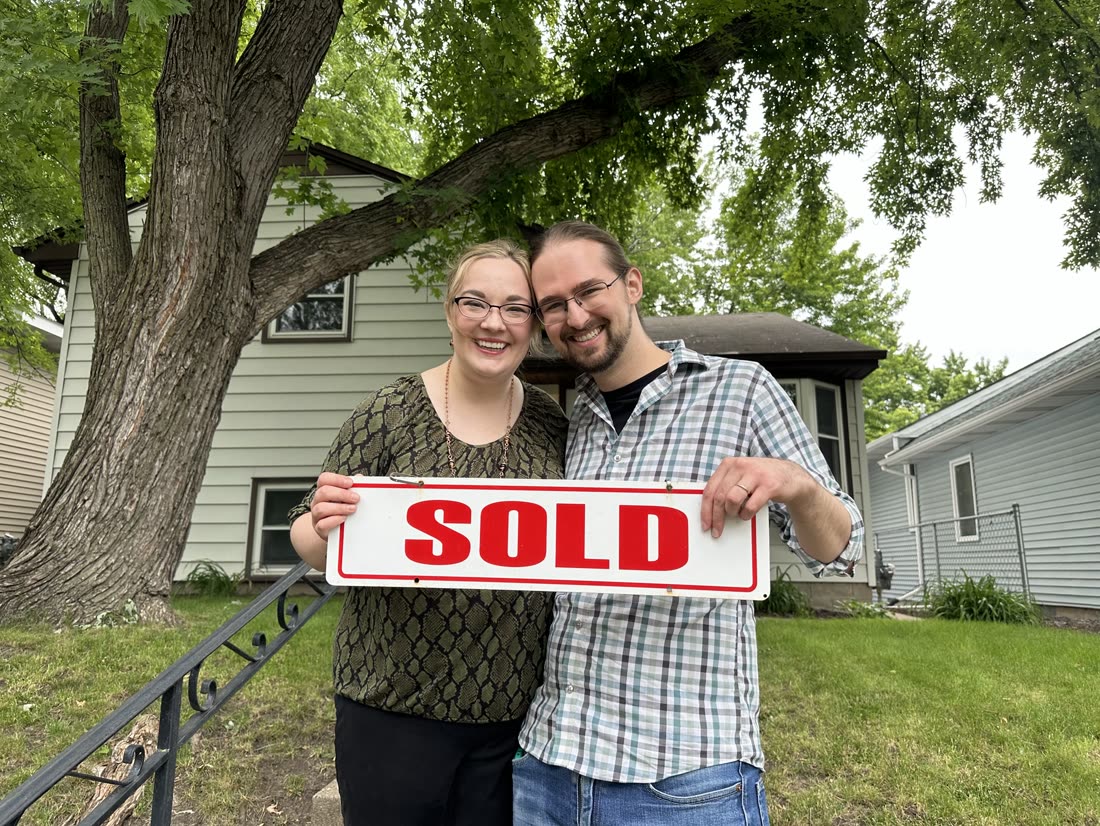 A couple holding a SOLD sign in front of their new home