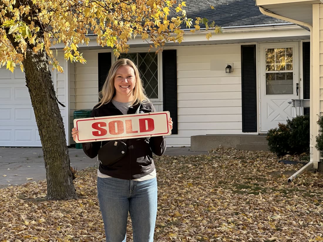 A client holding a SOLD sign in front of her new home