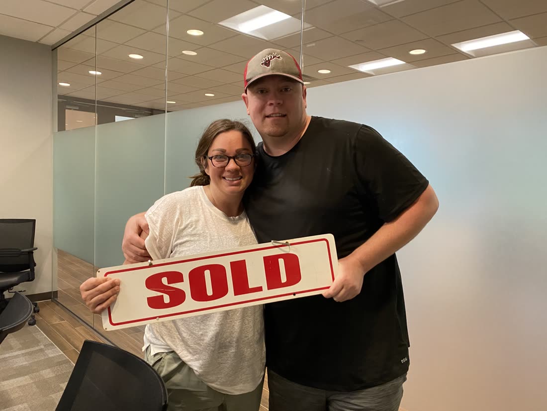 A couple holding a SOLD sign on closing day